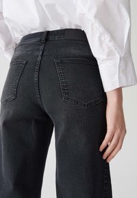 Jeans en denim noir taille haute avec une coupe slim, dotés de deux poches arrières et d'une ceinture lisse. La texture semble légèrement douce.