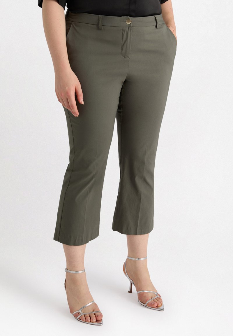 Pantalons cropped vert olive en tissu léger, avec un bouton à l'avant, des passants de ceinture et des poches. Assortis à des escarpins argentés à lanières.