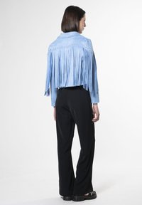 Giacca di suede blu chiaro con lunghe frange lungo la schiena e le spalle, abbinata a pantaloni neri e sandali neri chunky.