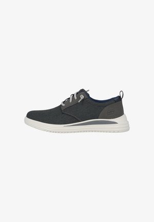 Zapatilla textil gris con cordones gris claro, suela blanca y un acento azul marino en el talón. Presenta un diseño simple y una parte superior texturada.