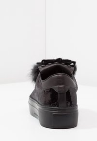 Schwarzer Sneaker mit Paillettenstruktur, weichem Fellbesatz an der Ferse, flacher Gummisohle und Schnürdesign. Sauberer, minimalistischer Stil.