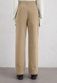Pantalons large beige en coton, dotés d'une poche au dos et d'une texture lisse, associés à des chaussures noires.
