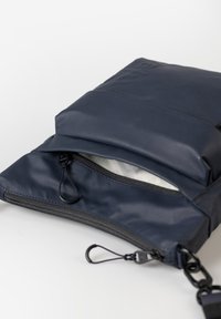 Borsa a tracolla compatta blu navy con due scomparti zip e tracolla nera regolabile su sfondo bianco.