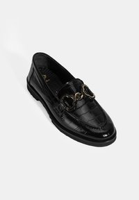 Zwarte leren instaploafer met een krokodillenpatroon, voorzien van een decoratieve ketting in goudkleur op de wreef en een ronde neus.