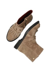 Bottines en suède beige avec des franges et un accent en anneau doré. Dotées d'une fermeture éclair sur le côté et d'une semelle en caoutchouc noir texturé.