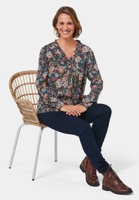 Blusa floreale con sfondo blu navy, caratterizzata da un collo a V e dettagli con bottoni, abbinata a jeans blu scuro e stivaletti marroni con lacci.