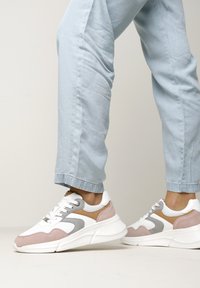 White and grey sneaker with pink suede accents. Featuring mesh panels, a padded collar, and a thick white sole. Worn with light blue jeans.