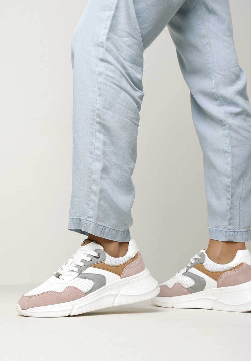 White and grey sneaker with pink suede accents. Featuring mesh panels, a padded collar, and a thick white sole. Worn with light blue jeans.