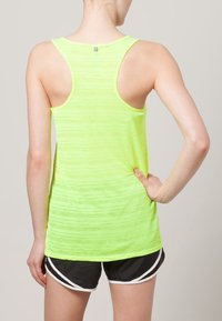 Neonowo żółty sportowy tank top z wycięciem typu racerback; wykonany z lekkiego materiału o subtelnej fakturze, w połączeniu z czarnymi szortami.