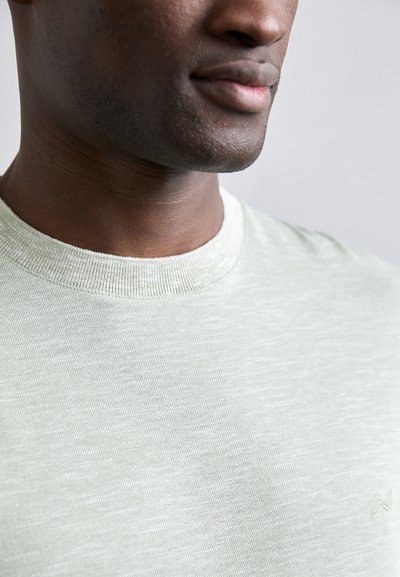 Lys grønn t-skjorte med rund hals laget av myk stoff med en subtil tekstur. Har en ribbestrikket halslinning og en liten brodert logo på siden.