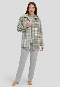 Chaqueta de forro polar a cuadros en gris y amarillo sobre una blusa gris clara con patrón de puntos. El modelo lleva pantalones grises a juego. Textura suave y material blando.