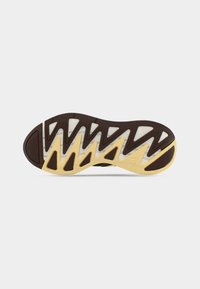 Jalatsi talla, millel on jaotatud disain, pruun kumm kollaste aktsentidega ning valged polsterduspaneelid; tekstureeritud haarde ja paindlikkuse tagamiseks.