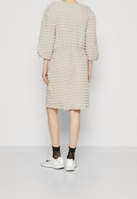 Beige kuvioituneella kankaalla varustettu mekko, jossa on puffimaiset hihat ja kapea vyötärö, yhdistetty valkoisiin lenkkareihin ja mustiin kuvioituihin sukkiin.