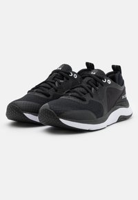 Svarta träningsskor med en strukturerad mesh-övre, solida svarta accenter, vit mellansula och en gummiyttersula med honungscomb-mönster.