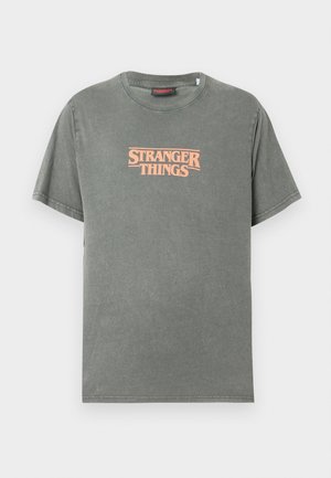 Σκούρο πράσινο βαμβακερό T-shirt με κοντά μανίκια, με λογότυπο "STRANGER THINGS" σε ροζ απόχρωση και ρετρό γραμματοσειρά που κε�ντράρεται στο στήθος.