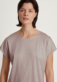 Top leggero e stampato con un design geometrico nei colori rosa e verde. Presenta un collo rotondo e maniche corte e ampie, realizzato in tessuto traspirante.