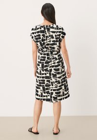 Černobílé šaty s volným střihem, stojatými rukávy a páskem na zavázání v pase, vyrobené z lehké tkaniny.