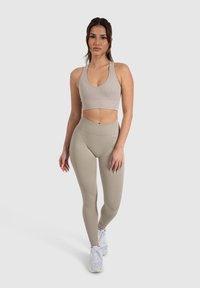 Top sportivo beige a coste e leggings a vita alta abbinati, realizzati in tessuto elastico, abbinati a sneakers bianche. Design semplice e aderente.