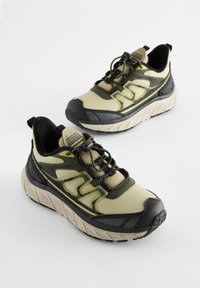 Sportowe sneakersy z jasnoliwym wierzchem, czarnymi akcentami, teksturowaną siateczką, grubą amortyzującą podeszwą oraz odblaskowymi sznurowadłami.