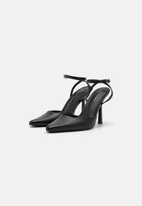 Sapatos de salto alto em couro preto com bicos pontiagudos, tiras no tornozelo e um design elegante. Textura lisa com um acabamento polido.