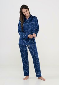 Conjunto de pijama en azul marino de material suave, con un patrón de estrellas blancas, camisa de botones con bolsillo y pantalones a juego con cintura ajustable.