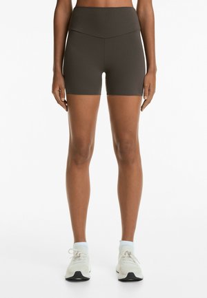 Brown, high-waisted athletic shorts with a smooth texture, fitted design, and mid-thigh length, paired with light sneakers and socks.