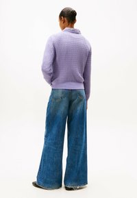 Liliowy sweter z dzianiny o teksturowanym wzorze, w połączeniu z szerokimi, wyblakłymi niebieskimi dżinsami. Strój charakteryzuje się żebrowanymi brzegami i surowymi wykończeniami.