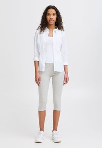 Chemise blanche à boutons, leggings gris jusqu'aux genoux et baskets blanches. La chemise a un design à col, tandis que les leggings ont une apparence texturée.