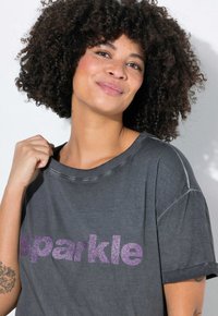 Grå kortærmet t-shirt med rund halsudskæring, der har et glitrende lilla "sparkle" grafisk print på forsiden. Blødt, struktureret stof.