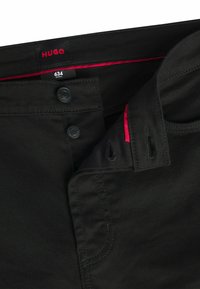 Sorte tapered bukser med HUGO-etiket, der har to sorte knapper, røde detaljer indeni taljebåndet og subtile syninger.