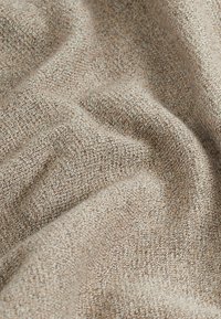 Beige textured fabric with a woven pattern, displaying soft, draped folds. The material has slight variations in color.
