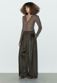 Brązowy żebrowany kardigan z długim rękawem i guzikami, w połączeniu z wysokim stanem, szerokimi spodniami w kolorze ciemnego brązu z satynowego materiału. Gładka tekstura.