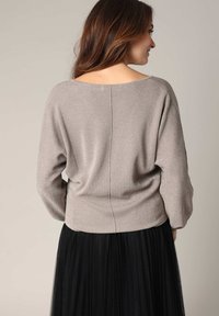 Pull en maille gris clair avec une coupe décontractée, un col large et une texture côtelée, associé à une jupe plissée noire fluide.