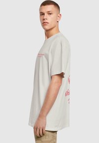 Lys grå bomulds t-shirt med løs pasform, korte ærmer, rød trykt tekst foran og bagpå, rund halsudskæring og glat tekstur.
