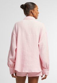 Světle růžová bavlněná košile s texturovaným, zmačkaným povrchem; oversize střih, dlouhé rukávy, zapínání na knoflíky na manžetách a límec s rozparkem.