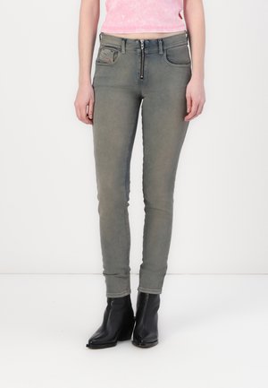 Gray skinny jeans made of denim, featuring a zip fly, front pockets, and subtle stitching details. Worn with black ankle boots.