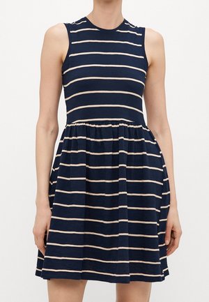 Sukienka bez rękawów w kolorze granatowym z beżowymi poziomymi paskami, dopasowanym gorsetem, marszczoną talią i rozkloszowanym dołem, noszona przez stojącą osobę.