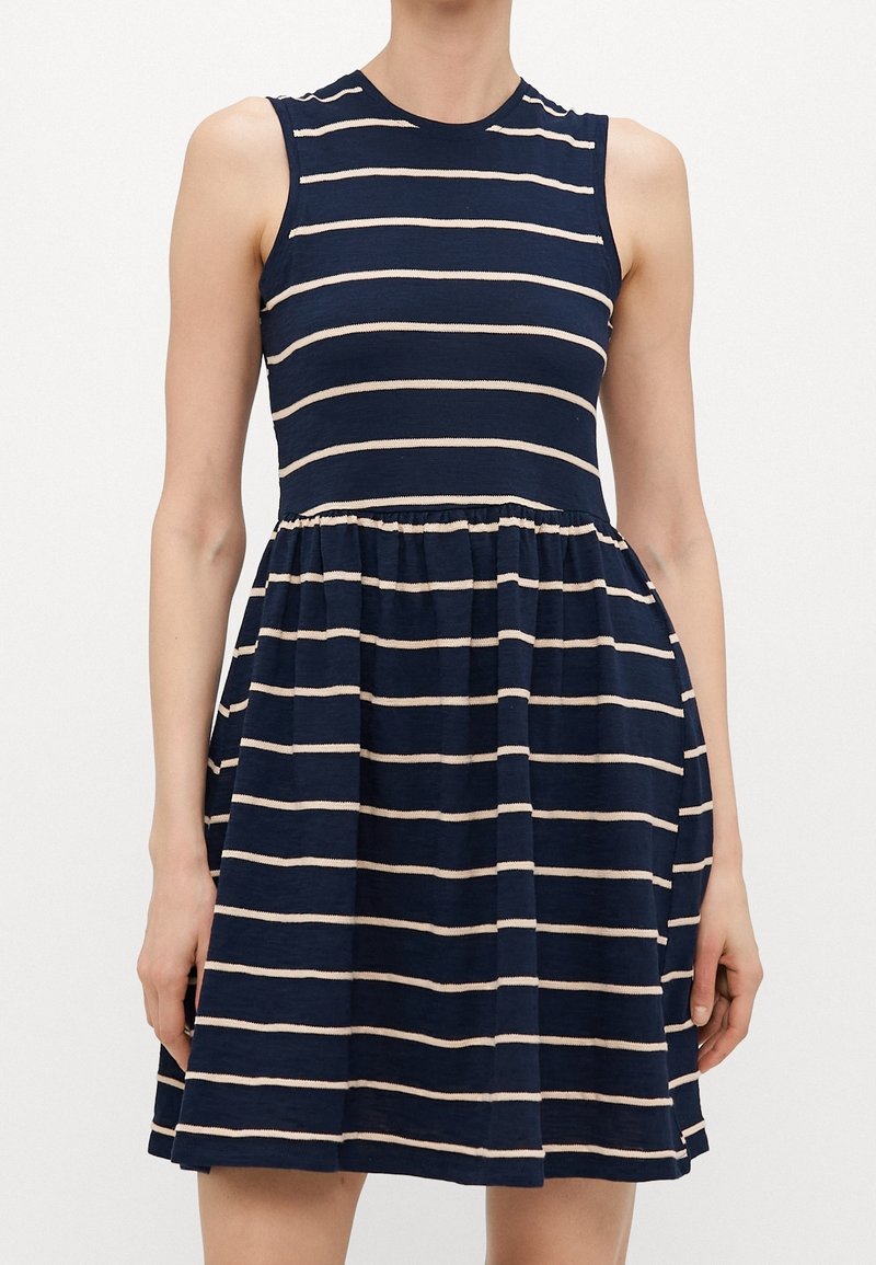 Robe bleu marine sans manches avec des rayures horizontales beiges, corsage ajusté, taille froncée et jupe évasée portée par une personne debout.