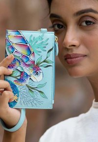 Een lichtblauwe portemonnee met een kleurrijk schildpadontwerp, omringd door waterplanten, gedetailleerd met ingewikkelde patronen en een ritsluiting.