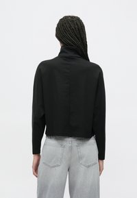 Černé, krátce střižené tričko s dlouhým rukávem a vysokým límcem, vyrobené z měkké látky. Doplněné světle šedými širokými džíny s kapsami na zadní straně.