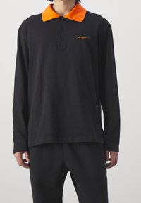 Polo shirt nero a maniche lunghe con colletto arancione, dotato di una pattina con quattro bottoni e delicata ricamatura del logo arancione. Materiale in cotone morbido.