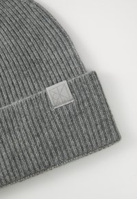 Γκρι πλεκτό σκουφάκι φτιαγμένο από μαλακό υφασμάτινο υλικό. Διαθέτει ριμπέ σχέδιο και μια ορθογώνια γκρι ετικέτα με λογότυπο στην διπλωμένη άκρη.