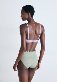 Σουτιέν με ανοιχτό μωβ τιράντες και πλέγμα στην πλάτη, συνδυασμένο με ψηλόμεσα, ανοιχτό πράσινα υφασμάτινα εσώρουχα με λοξό κόψιμο.