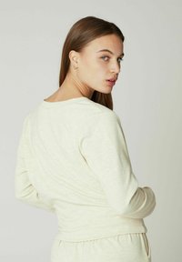 Chemise à manches longues beige clair en tissu doux, dotée d'un col rond et d'une silhouette ajustée avec des poignets côtelés.