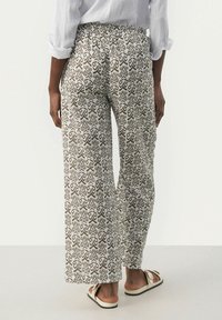 Witte, lichte, wijde broek met een bruin, draaiend patroon; voorzien van een elastische tailleband en een relaxed fit. Zichtbaar van de achterkant.