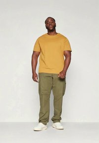 Sinapin keltainen t-paita, oliivinvihreät cargo-housut ja valkoiset lenkkarit. Yksinkertainen muotoilu, pyöreä pääntie ja sivutaskut housuissa.