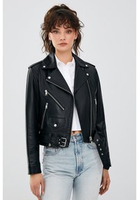 Zwarte leren motorjack met een getailleerd ontwerp, ritszakken en zilverkleurige hardware. Gecombineerd met lichtblauwe high-waisted jeans.