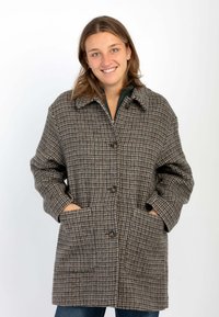 Giacca a quadri marrone, crema e grigio. Presenta un colletto, bottoni frontali e ampie tasche laterali. Realizzata in tessuto testurizzato.