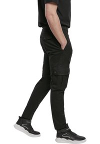 Černé cargo kalhoty slim fit, s bočními kapsami a knoflíkovými detaily. Vyrobeno z odolného materiálu, v kombinaci s černými vysokými teniskami.