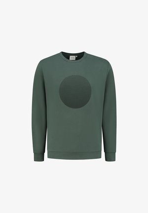 Zaļš džemperis, izgatavots no mīkstas auduma, ar teksturētu apļa dizainu priekšpusē. Apaļš kakls un ribota piegriezuma piedurknes un apakša.